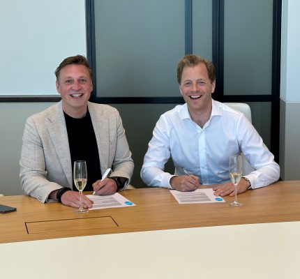Twee mannen ondertekenen een overeenkomst, met een glas champagne naast zich